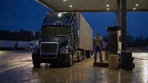 diesel prices truck drivers — a driver fueling a dark blue semi truck at a truck stop fuel island at night
