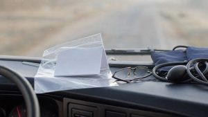 paper medical card — a folded card in a plastic sleeve, reading glasses and a blood pressure cuff on a truck dashboard
