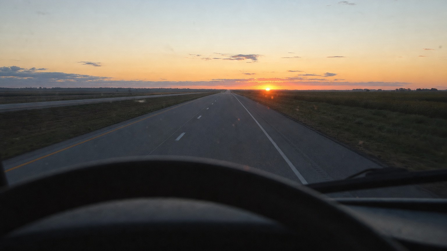 time zones for truck drivers — view through a truck windshield of an empty interstate at sunrise with the steering wheel in the foreground