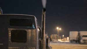 truck idling laws — exhaust vapor rising from the chrome stack of a parked semi truck at a winter truck stop at night
